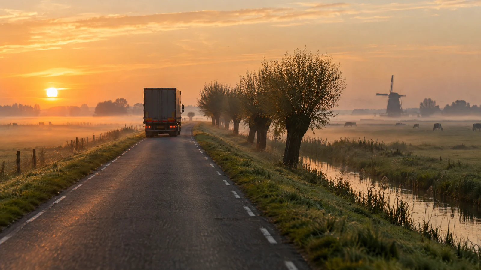 Vrachtwagen op een polderweg bij zonsopgang, laaghangende mist boven de weilanden